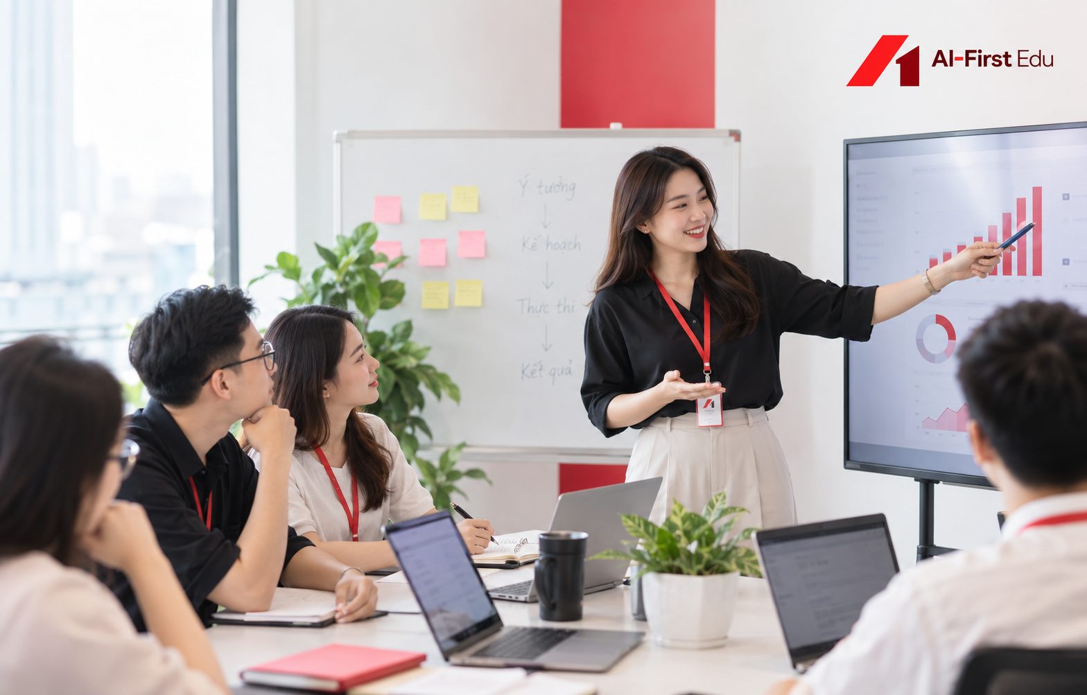 Giảng viên trình bày kết quả trên màn hình cho lớp học đang ngồi theo dãy bàn